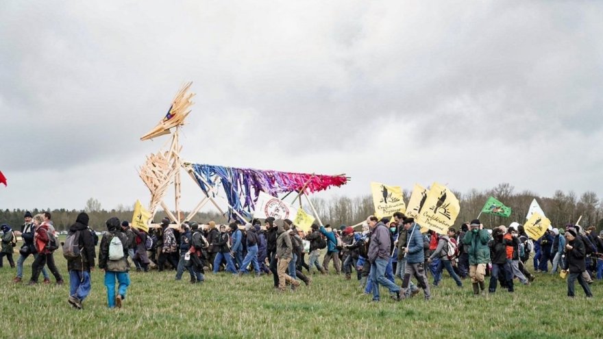 Demonstranter som går på et jorde, med en stor trefigur og bannere fra Les soulèvements de la terre.